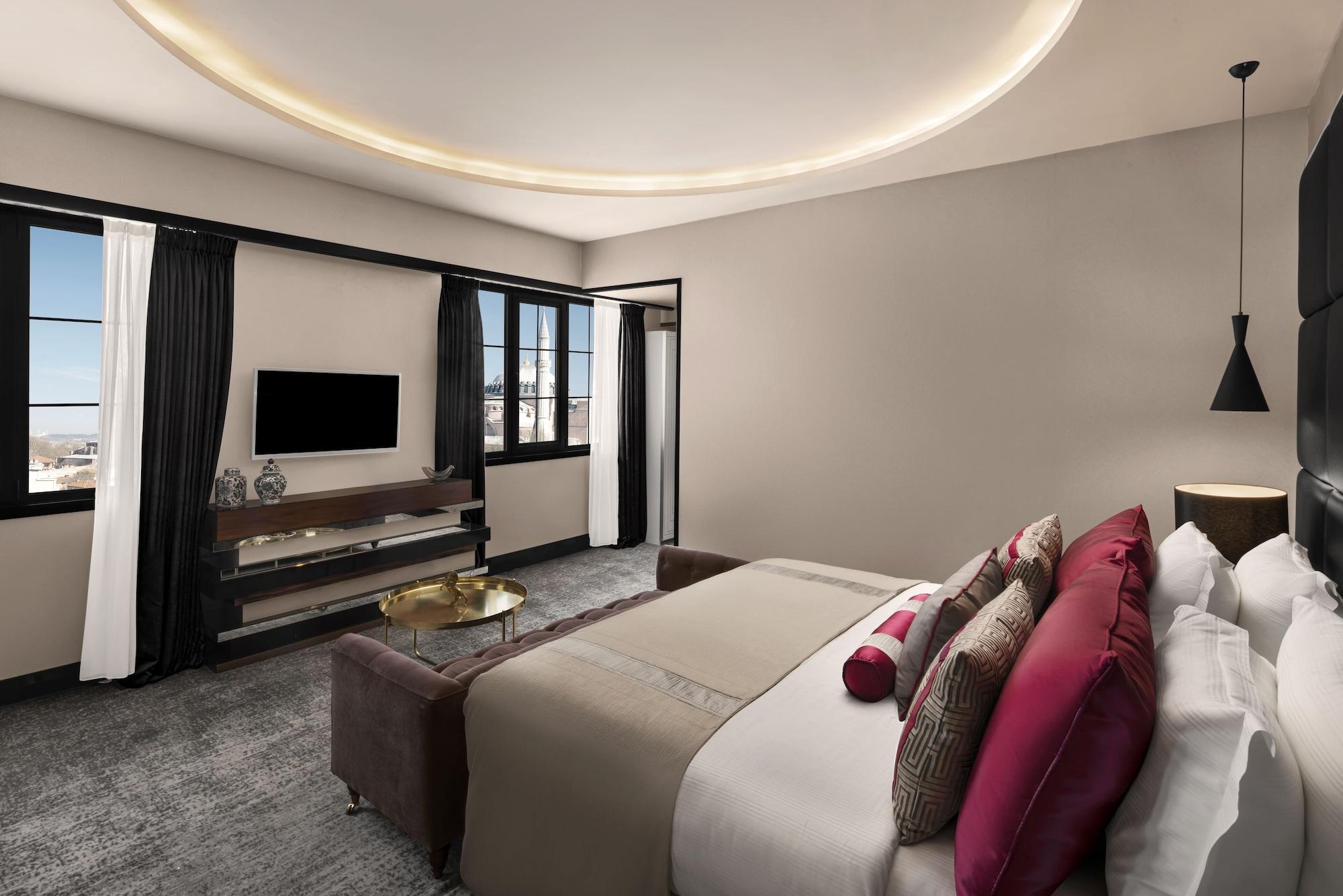 Sura Hagia Sophia Hotel Istanbul Exteriör bild The photo shows a modern hotel room. It features a large bed adorned with decorative pillows in shades of pink and neutrals. There is a sleek wooden console beneath a flat-screen television mounted on the wall. The room has large windows with flowing