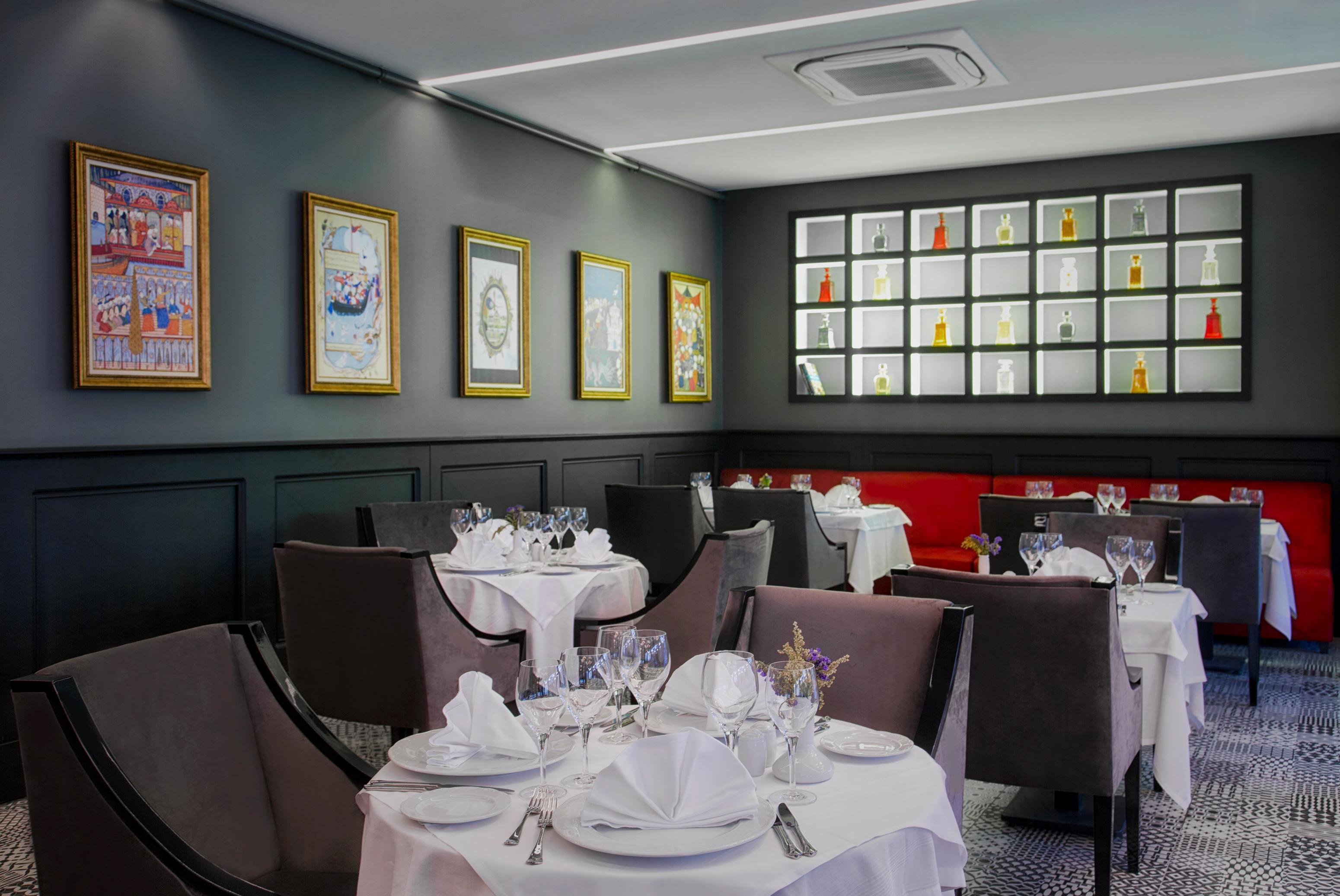Sura Hagia Sophia Hotel Istanbul Exteriör bild The photo shows a stylish restaurant interior. The space features dark walls adorned with framed artwork, including colorful paintings in gold frames. There are neatly set tables covered with white tablecloths, each featuring elegant glassware and fo
