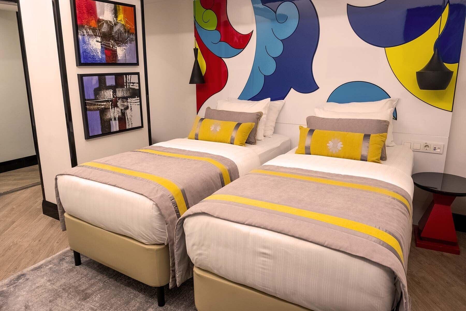 Sura Hagia Sophia Hotel Istanbul Exteriör bild The photo shows a modern hotel room featuring two single beds with light-colored linens and decorative yellow-striped throw pillows. The headboards of the beds are against a colorful mural that includes abstract shapes in red, blue, and yellow. To th